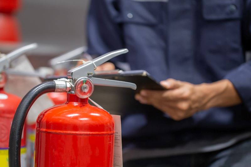 A man holding a clipboard is inspecting a red fire extinguisher